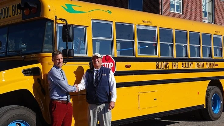 Handshakes and smiles next to the Bellows Free Academy, Fairfax EV Bus.