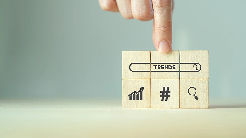 A finger points to wooden blocks with the word "trends," a hashtag symbol, a magnifying glass, and a growth chart symbol printed on them in black
