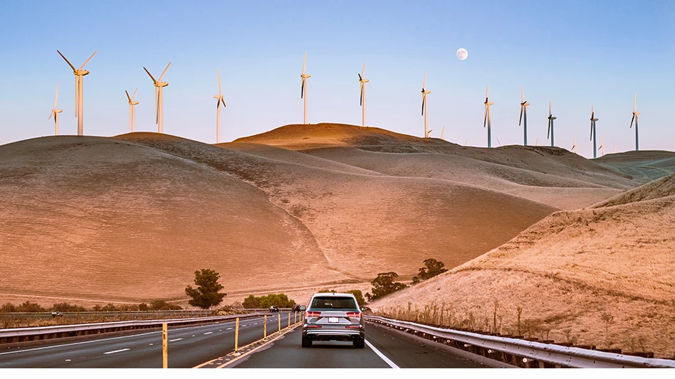 A car drives down a road with windmills in the distance