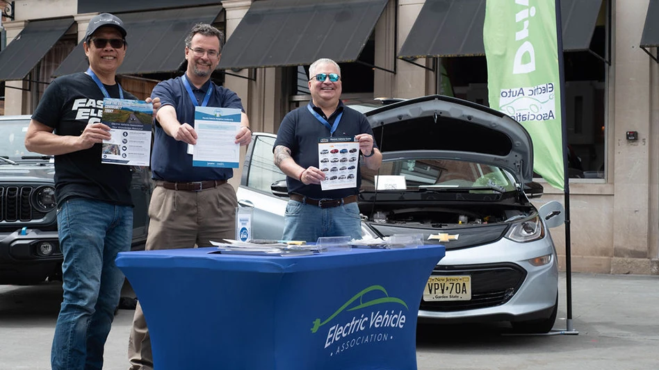 Three people behind a table with cars in the background