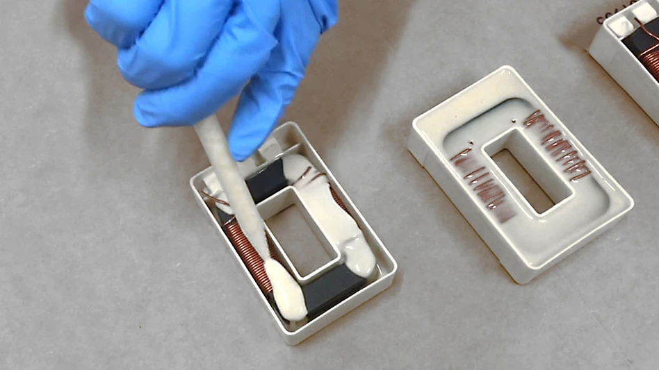 A blue gloved hand applies a resin to a part