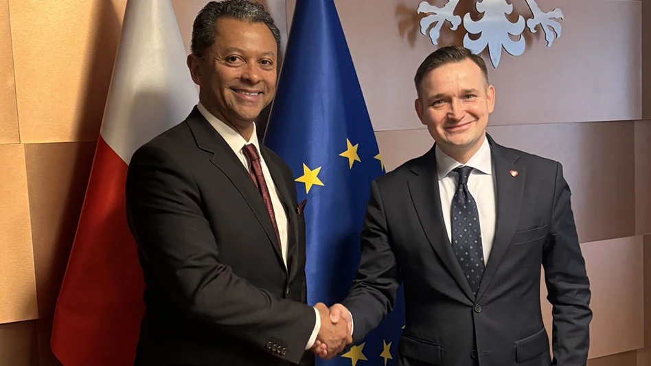 Two people shaking hands in front of a pair of flags