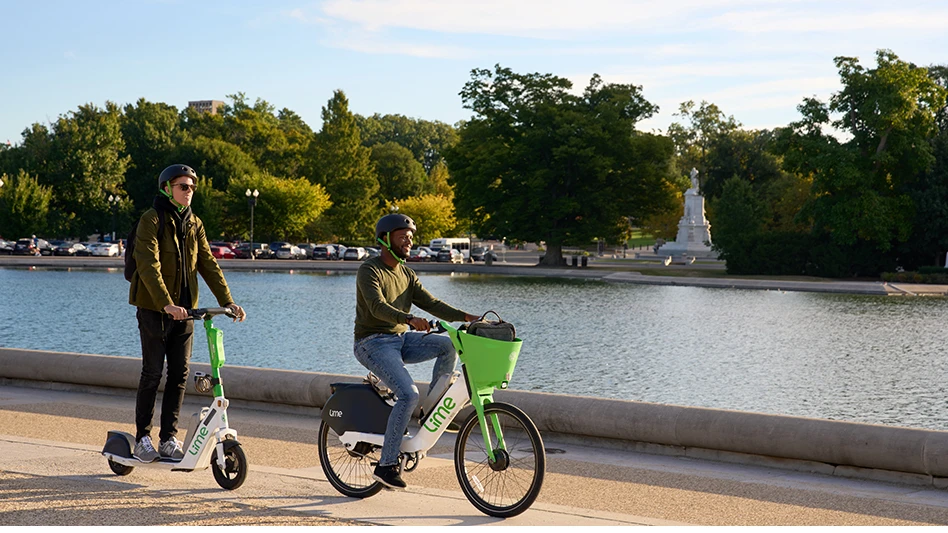 A person riding a bike and a person riding a scooter next to a river