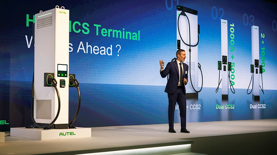 A person standing onstage with electric vehicle chargers